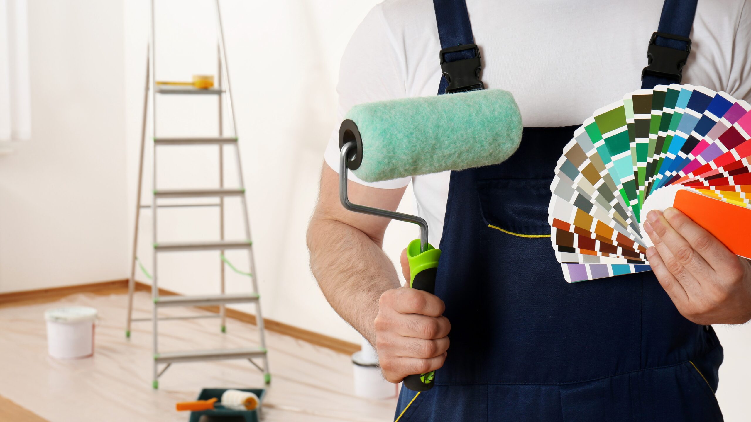 Male painter holding color palettes and paint roller, with ladder in background