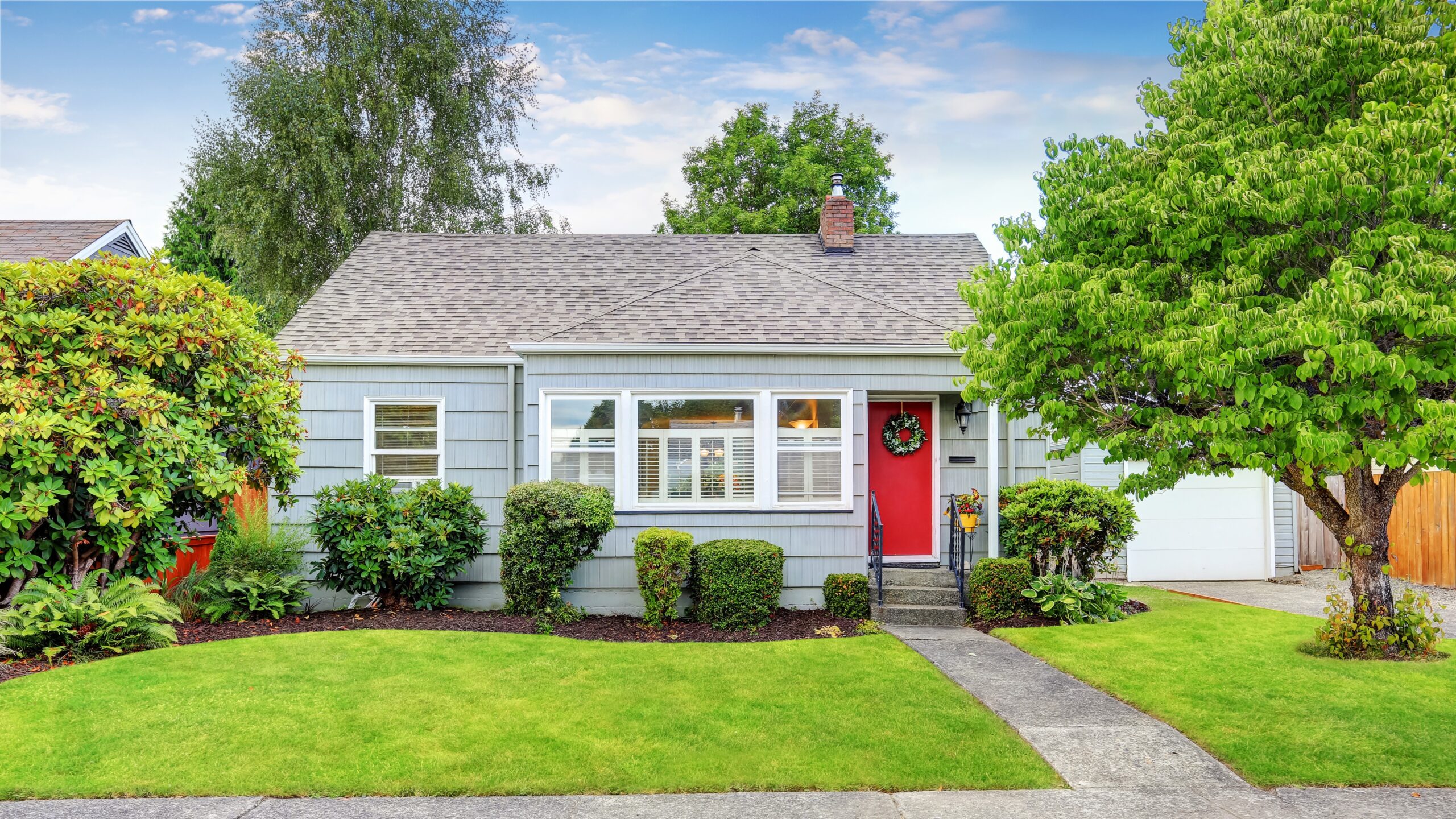 Small American house with light blue exterior, red door, concrete walkway, and freshly landscaped front yard