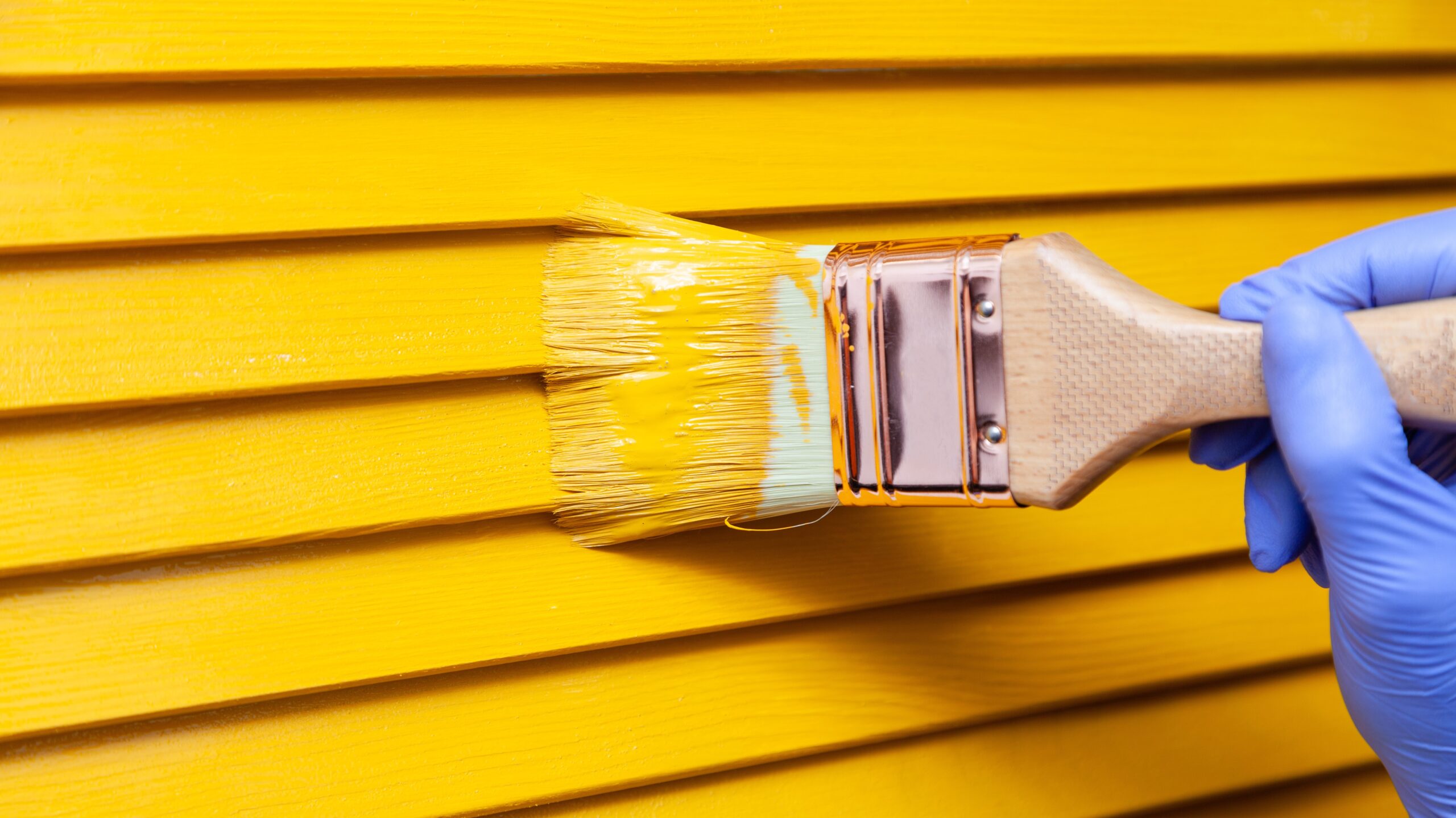 Close up of painter’s hand in purple glove painting siding in yellow