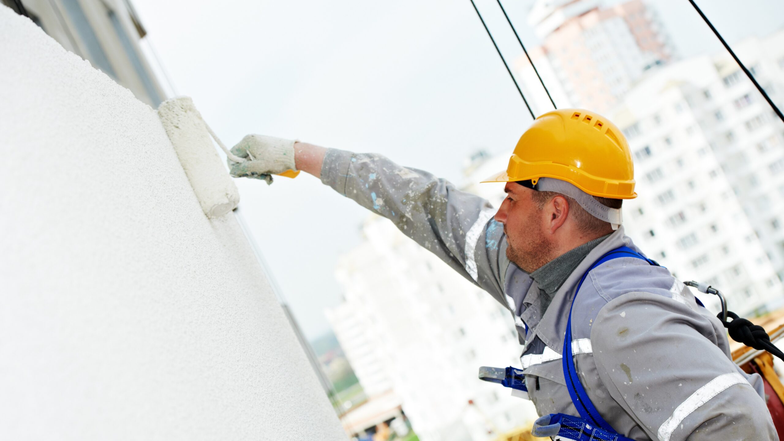 Single male painter using paint roller on house facade to give it a white color