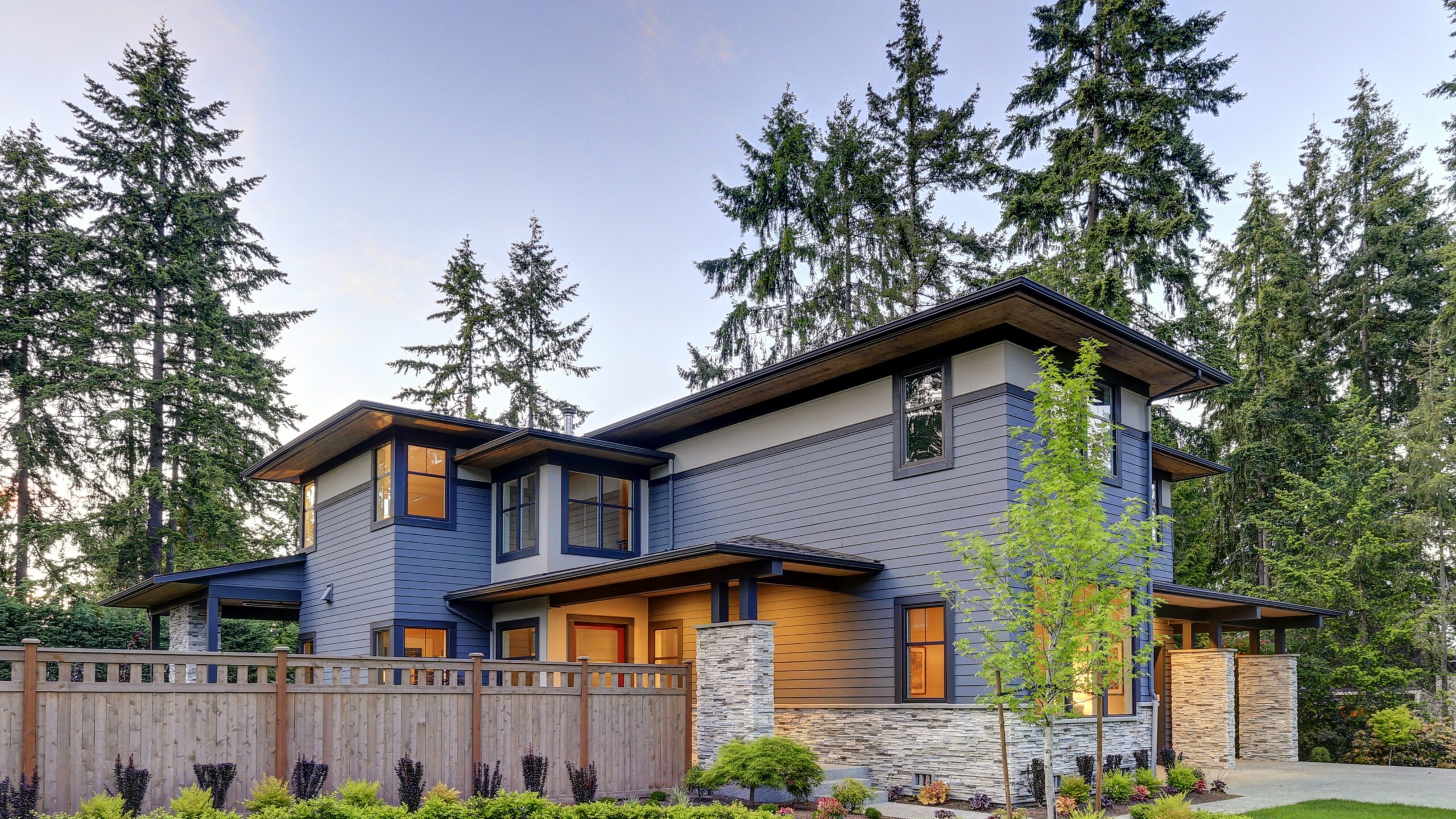 Contemporary home with blue siding with wooden fence and illuminated windows