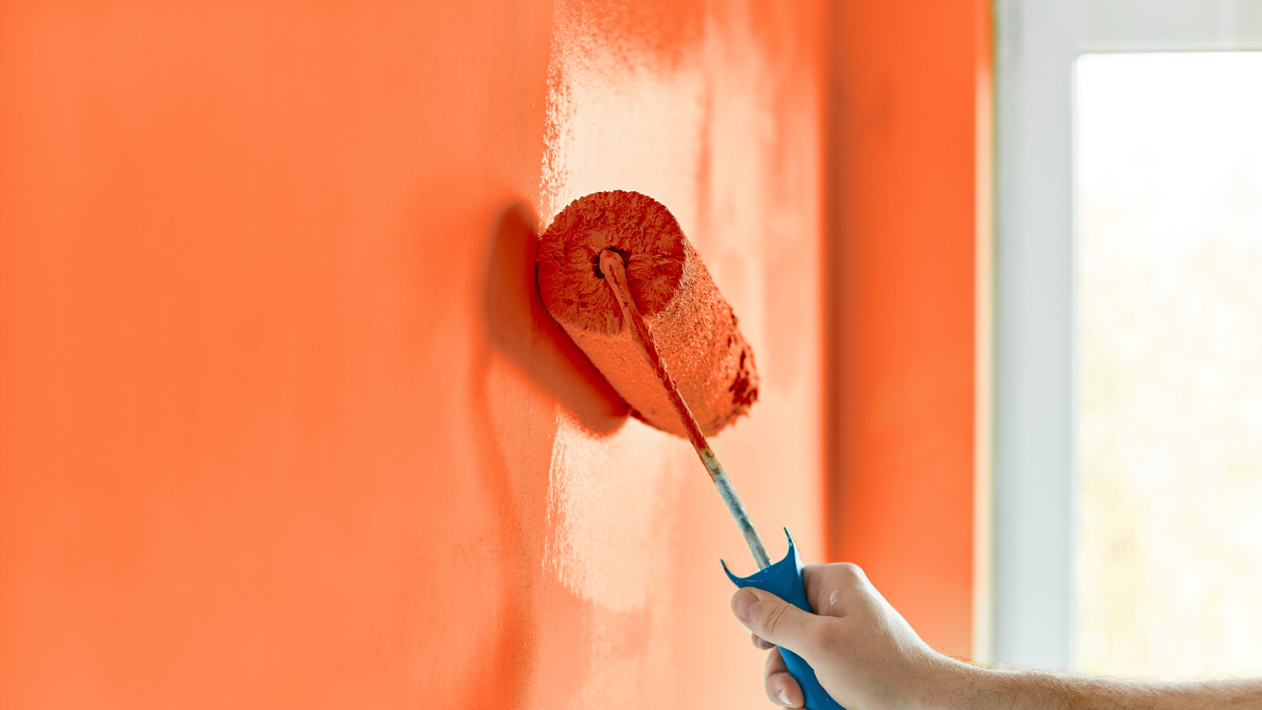 Male hand painting wall with paint roller. Painting apartment, renovating with red orange color paint
