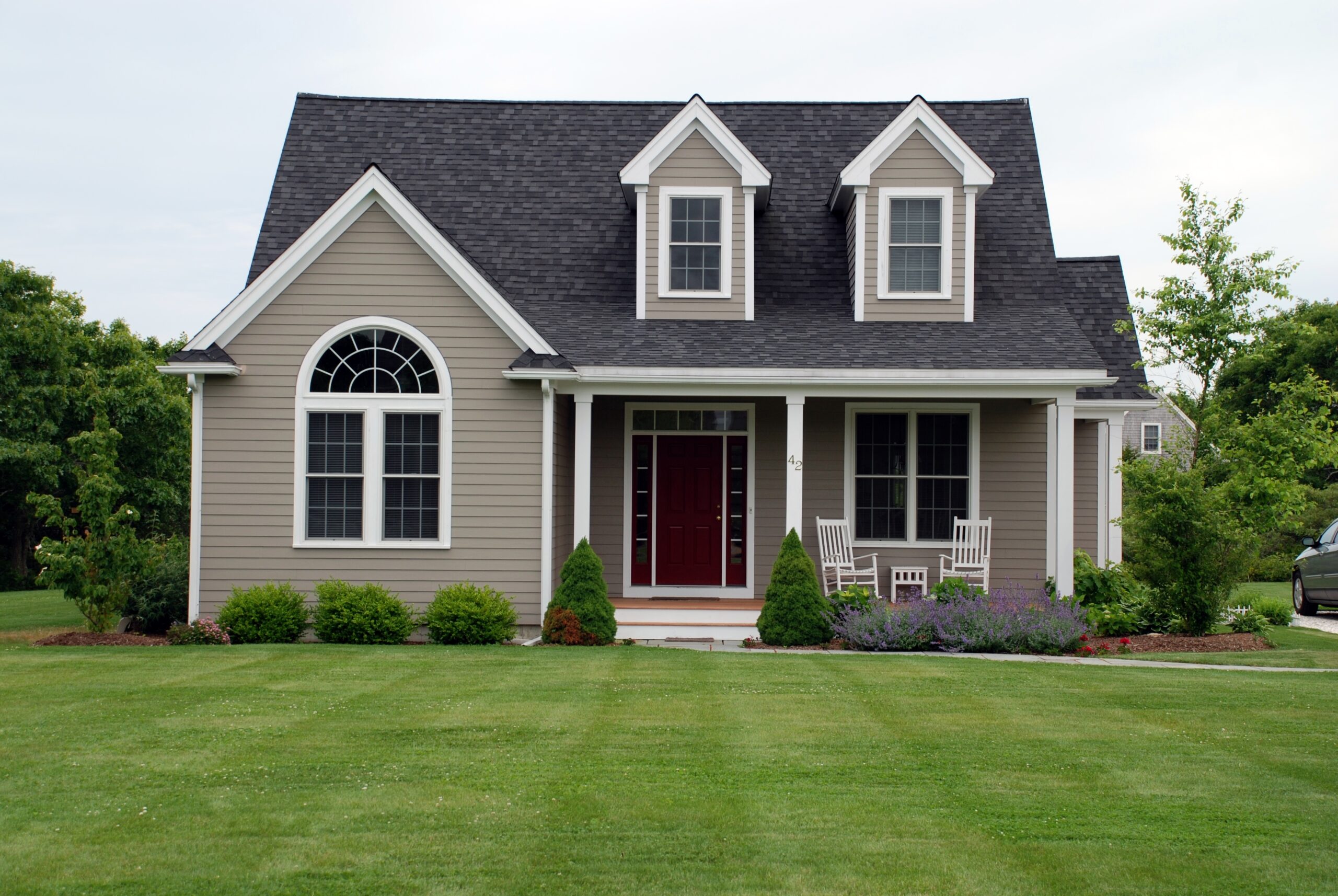 Two-story house with white rocking chairs and a freshly-cut front yard